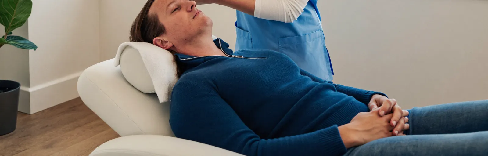A patient relaxing in a TMS treatment recliner while a clinician checks the setup