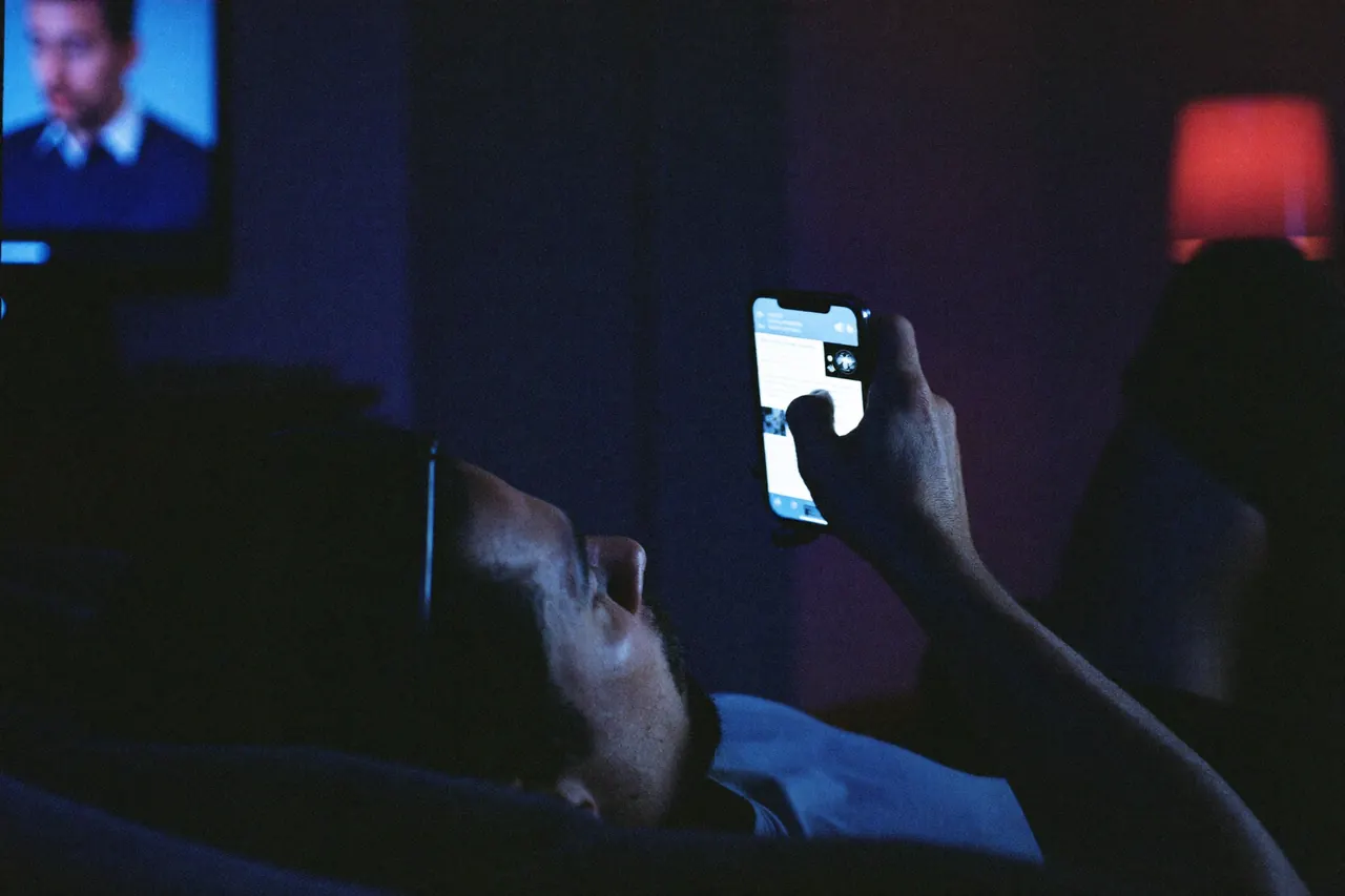 A man scrolling his phone on the couch in the evening