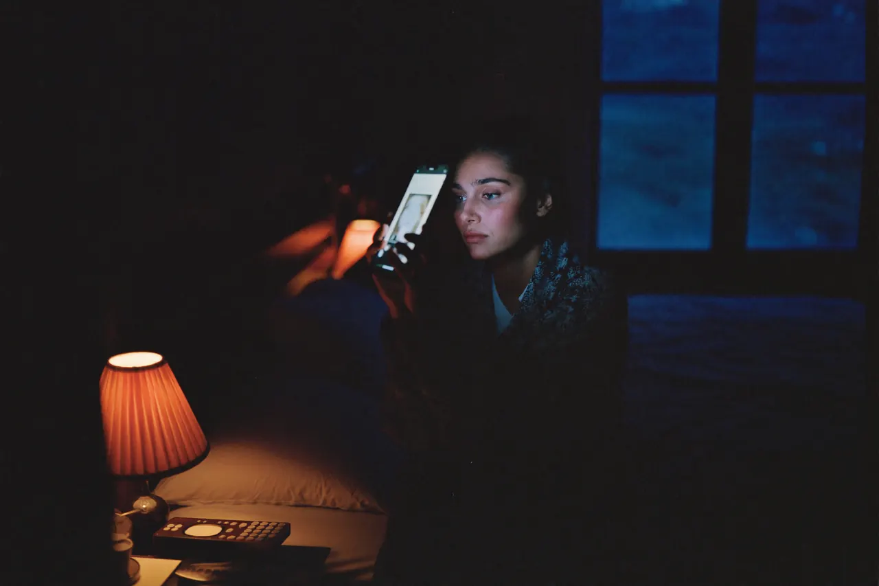 A woman reading her phone in a dark bedroom late at night